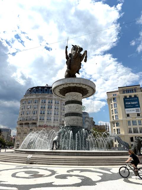       Grand equestrian fountain of Alexander the Great dominates Skopje’s main square under a bright sky.
  