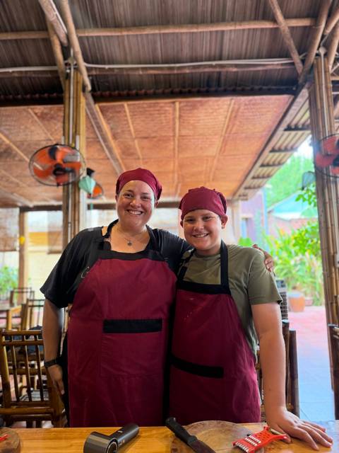       Mother and son wearing burgundy chef hats and aprons during a cooking class
  
