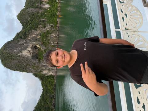       Boy flashing a peace sign on the deck of a cruise boat with limestone cliffs behind
  