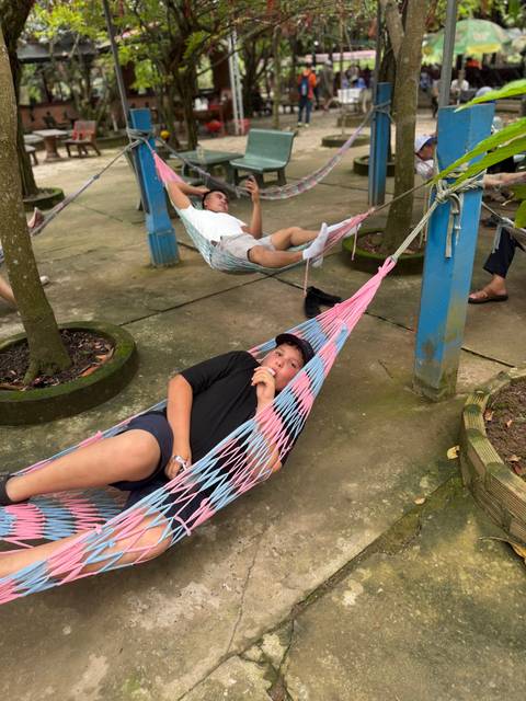       Boy lounging in a pastel-colored net hammock licking an ice cream in a shady courtyard
  