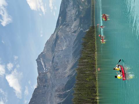       Colorful canoes with paddlers dot a bright turquoise lake surrounded by forested mountains.
  