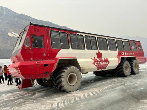       Large specialized Ice Explorer vehicle with maple leaf graphics parked on a glacier with visitors nearby.
  