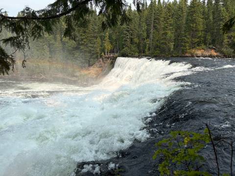       Powerful river waterfall crashing over a rocky ledge into mist with a partial rainbow.
  