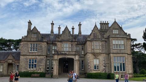       Historic manor house with ornate chimneys and visitors exploring the entrance courtyard.
  