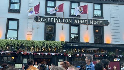       Crowd gathered outside Skeffington Arms Hotel and The Skeff Bar under hanging flower baskets.
  