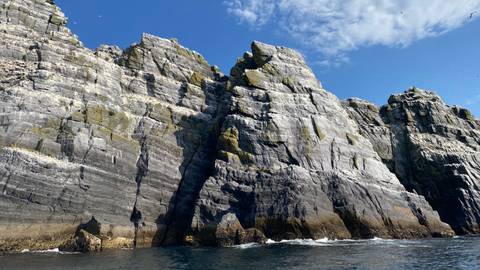       Towering grey sea cliffs rise sharply from deep blue Atlantic waters under a clear sky.
  