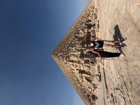       Two travellers standing before the Great Pyramid of Giza under a cloudless blue sky.
  