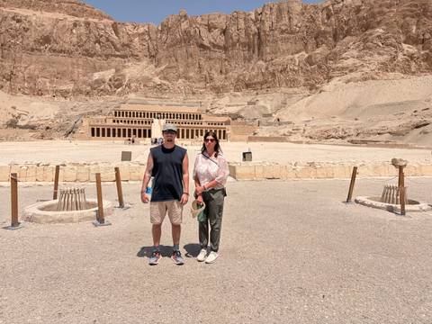       Travellers in front of the monumental Temple of Hatshepsut carved into desert cliffs under bright sun.
  