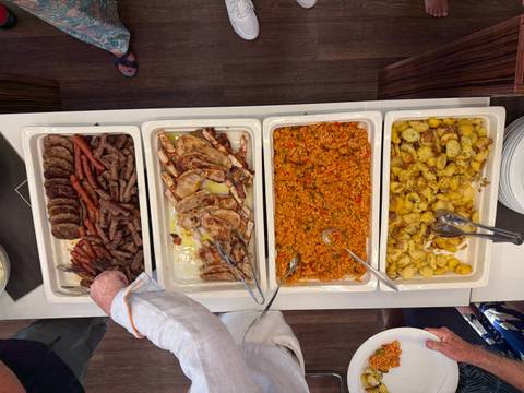       Overhead view of buffet trays filled with grilled meats, rice, and roasted potatoes being served.
  