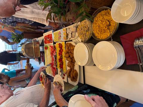       Guests queue at a breakfast buffet featuring fruit, pastries and cereals on a vessel’s deck.
  