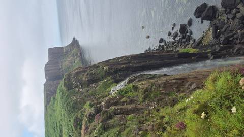       Tall coastal cliffs with Mealt Falls plunging into the sea near Kilt Rock on a cloudy day.
  