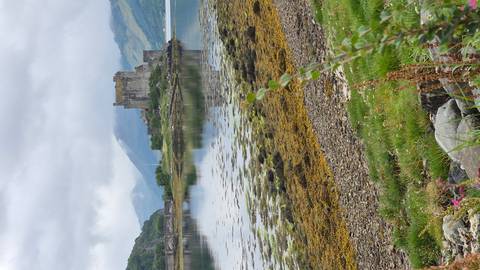       Eilean Donan Castle reflected in a still loch with seaweed-covered shore and misty highland backdrop.
  