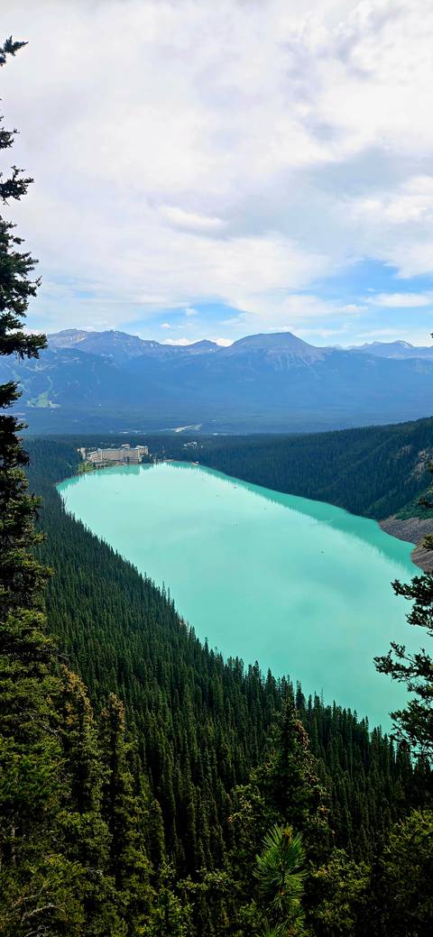       Elevated view of Lake Louise's turquoise expanse and iconic shore hotel nestled in forest.
  