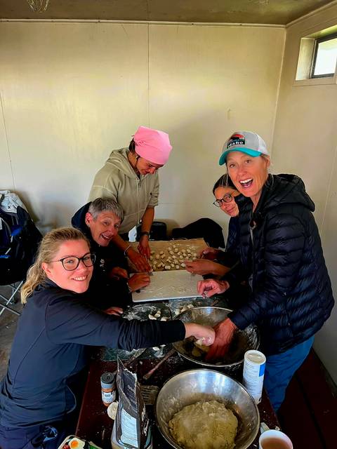       Group of campers joyfully prepare dumplings on a table inside a shelter.
  