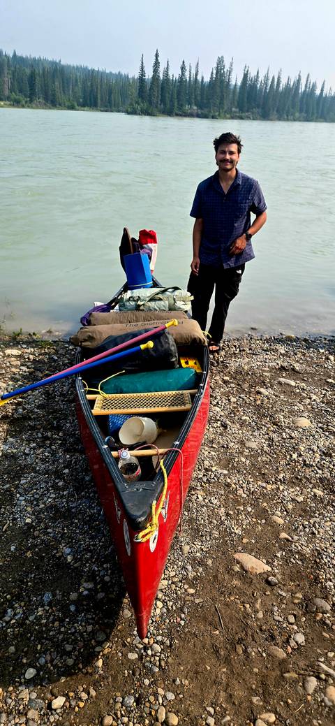       Canoe beached on a pebbled shore packed with dry bags, paddles and camping equipment next to turquoise water.
  