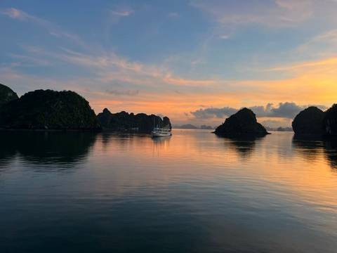       Serene sunset over limestone karst islands and a lone cruise boat in Halong Bay.
  