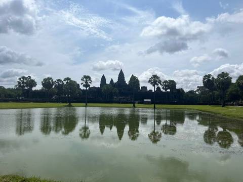       Reflection of the Angkor Wat towers in a calm moat beneath a partly cloudy sky.
  