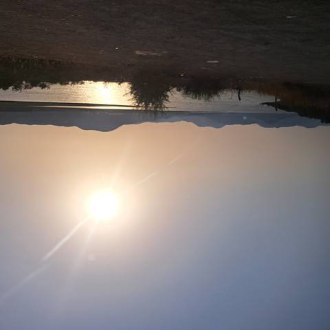       Setting sun casting golden light over a tranquil lake with distant rolling hills.
  