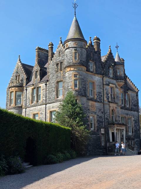       Elegant stone manor house with turrets and ornate windows against a bright blue sky
  