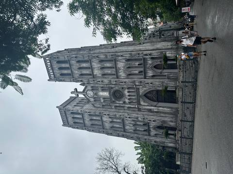       Gothic-style St. Joseph’s Cathedral towers over visitors walking past its weathered grey façade in Hanoi.
  