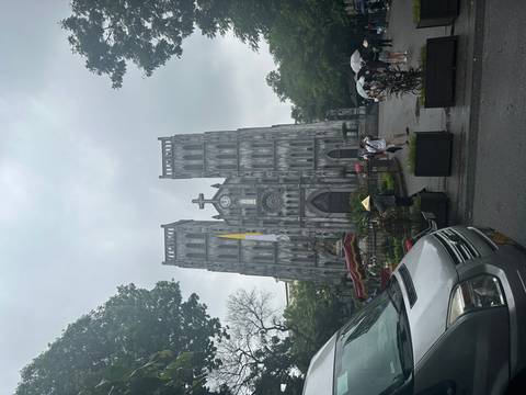       Front view of the grey neo-gothic cathedral with visitors and a parked van in the foreground
  