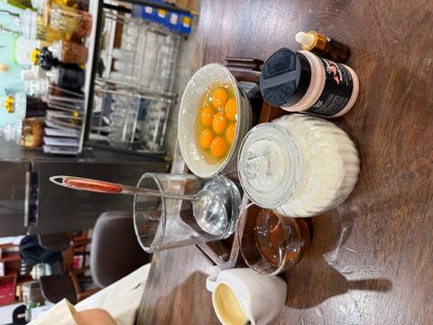      Tray of ingredients for egg coffee including raw egg yolks, condensed milk, honey and utensils on a café table.
  