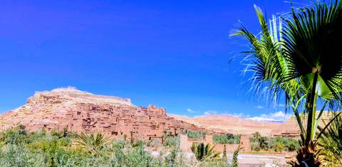       Ancient mud-brick citadel of Ait Benhaddou rises above a lush oasis under a deep blue sky.
  