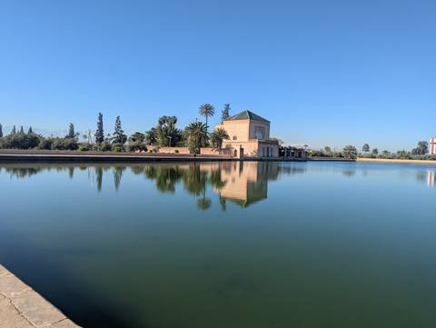       Pavilion of Marrakesh’s Menara Gardens reflected perfectly in a serene rectangular pool on a clear morning.
  