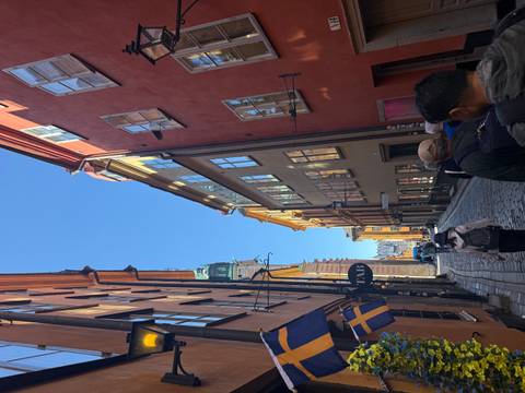       Sunlit cobblestone street lined with colourful historic buildings and Swedish flags in Stockholm’s old town
  