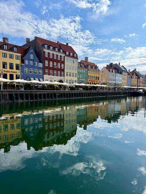       Iconic colourful townhouses of Nyhavn reflecting vividly in Copenhagen canal under blue sky
  