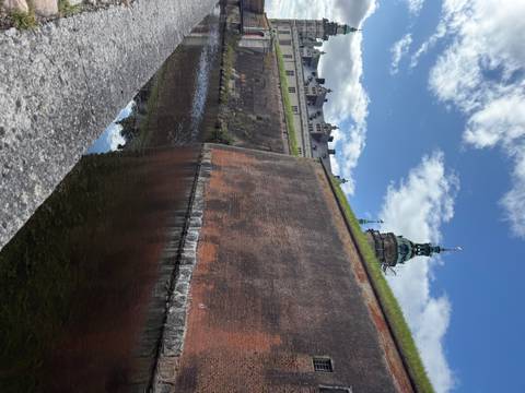       Massive red-brick ramparts and moat of Kronborg Castle with ornate tower rising beyond
  
