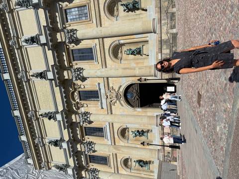       Visitor posing outside Stockholm Royal Palace with baroque façade and statues in bright sunshine
  