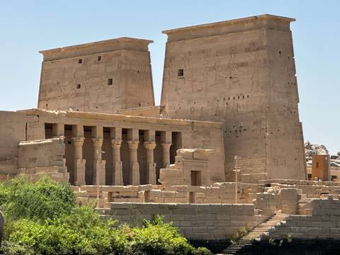       Temple walls of Philae with tall pylons etched with ancient Egyptian reliefs under bright sunlight.
  