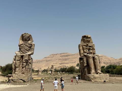       The Colossi of Memnon statues standing tall with arid mountains in the background.
  