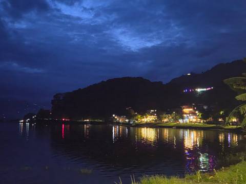       Evening view of lakeside town lights reflecting on calm water beneath deep blue sky.
  