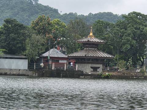       Small pagoda-style Barahi Temple on an island with forested backdrop and lake in foreground.
  