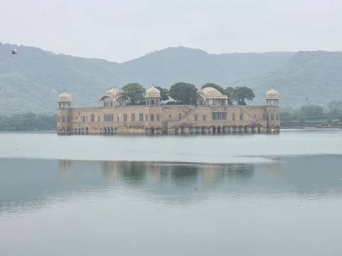      Jal Mahal palace floating in calm lake with misty hills in background.
  