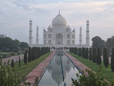       Symmetrical frontal view of Taj Mahal reflected in long pool at dawn.
  