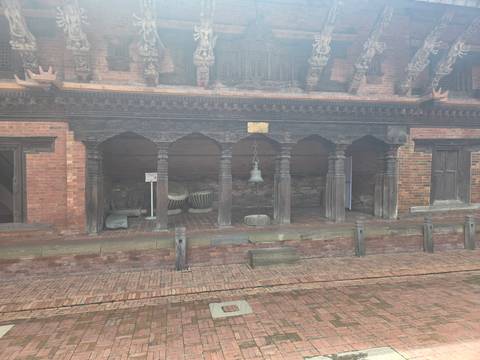       Brick and timber courtyard with bell and traditional Nepalese carvings partly veiled by mist.
  