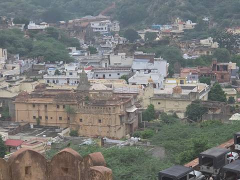       Elevated view across historic town with stone forts, temples and green trees.
  