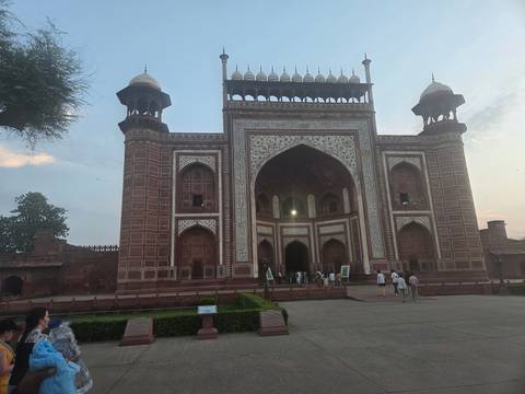       Grand Mughal gateway of Taj Mahal complex with tourists entering at dusk.
  