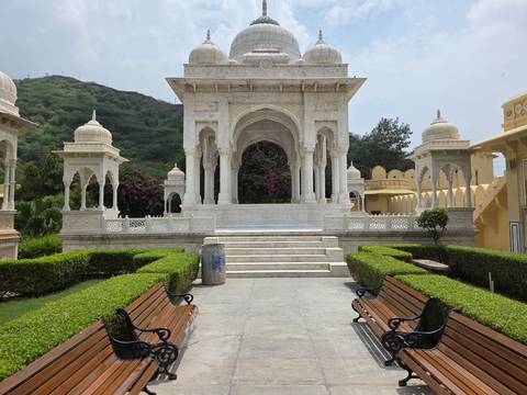       Elegant white marble cenotaph with manicured hedges and benches in foreground.
  