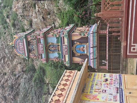       Colorful multi-tier Hindu temple tower set against rocky hillside.
  