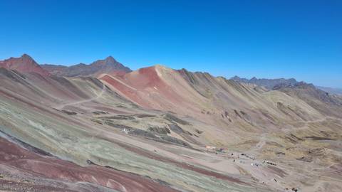       Panoramic view of the multicolored ridges of Peru’s Rainbow Mountain under clear blue skies
  
