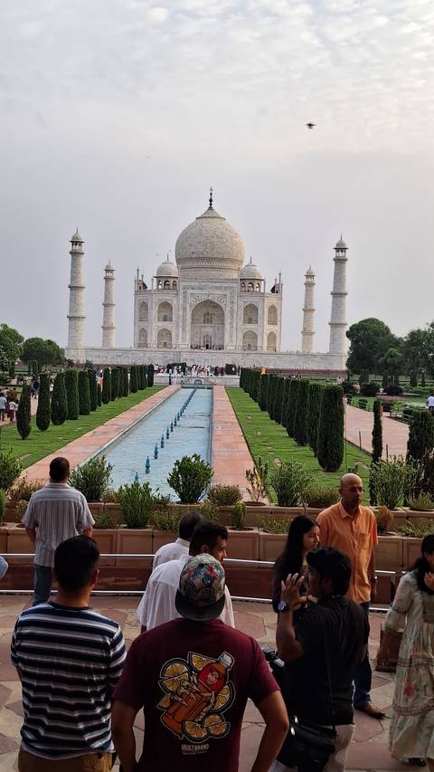       The iconic white marble Taj Mahal and its reflecting pool draw crowds on an overcast afternoon.
  