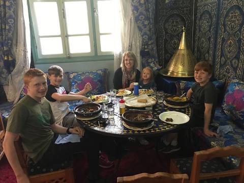       Family enjoys traditional Moroccan dishes around a round mosaic table in a richly decorated room.
  