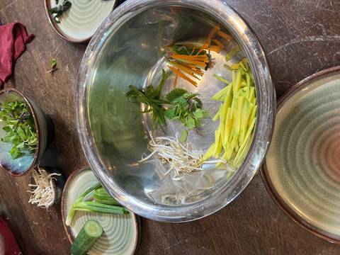       Metal mixing bowl and small piles of julienned vegetables and herbs prepared for cooking.
  