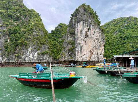       Small traditional boats float in emerald waters beneath towering limestone karsts.
  
