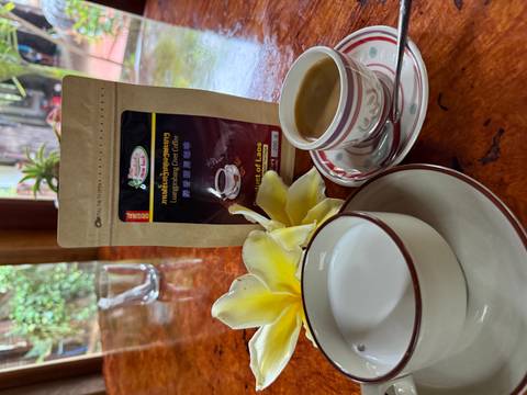       Cup of coffee beside a bag labeled 'Luangprabang Civet Coffee' on a polished wooden table.
  