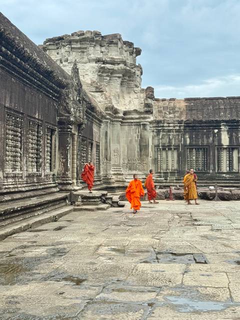       Buddhist monks in orange robes walk along the ancient stone galleries of Angkor Wat.
  